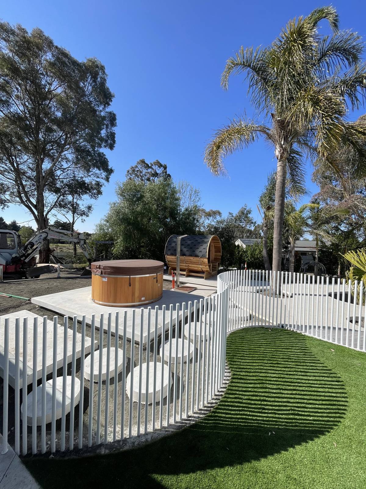 Curved white pool fence beside lawn and a wood fired hot tub